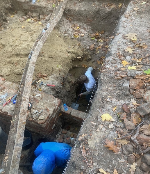 Researchers excavating the remains of a Warsaw Ghetto building in a narrow trench.
