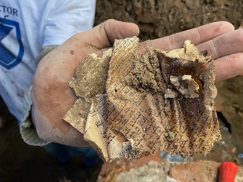 Fragment of a prayer book recovered during excavation, held in a researcher’s hand.
