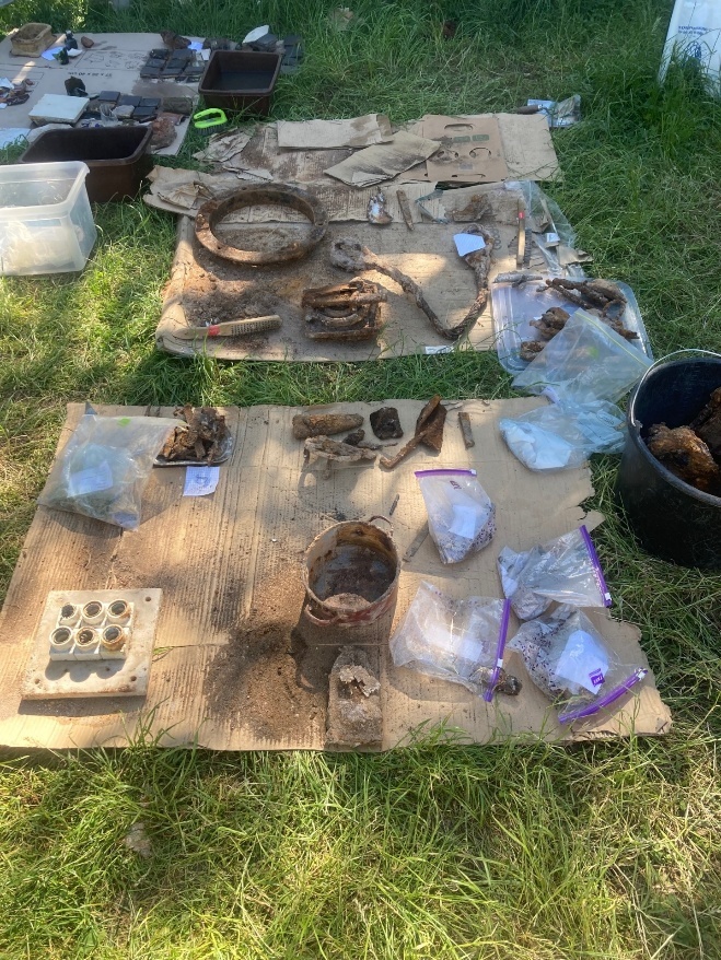 Artifacts recovered from the Mila 18 excavation arranged on tables outdoors.